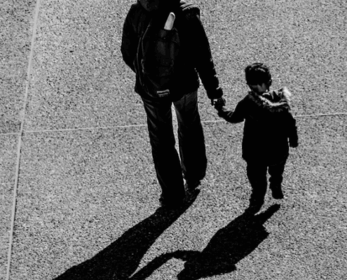 Mother and child on an open road, photographed from behind.